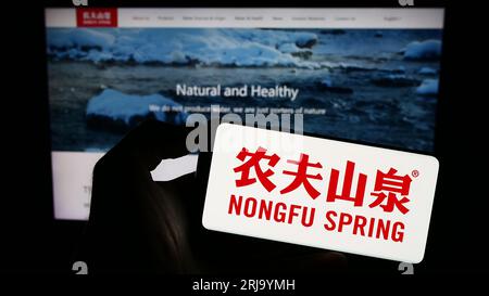 Person, die ein Smartphone mit dem Logo des chinesischen Unternehmens Nongfu Spring Company Limited auf dem Bildschirm vor der Website hält. Konzentrieren Sie sich auf das Display des Telefons. Stockfoto