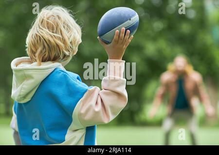 Rückansicht des kleinen Jungen, der mit seinem Vater im Park American Football spielt und Ball wirft, Kopierraum Stockfoto