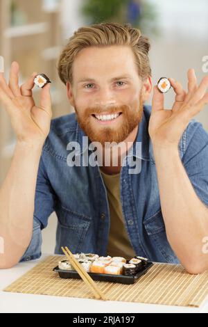 Glücklicher junger Mann, der Sushi-Brötchen hält Stockfoto