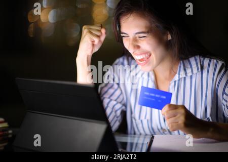 Begeisterte Frau, die abends zu Hause online mit Tablet und Kreditkarte kauft Stockfoto