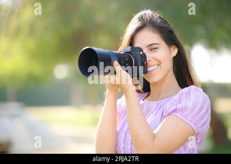 Glücklicher Fotograf, der mit einer spiegellosen Kamera arbeitet und Fotos in einem Park macht Stockfoto