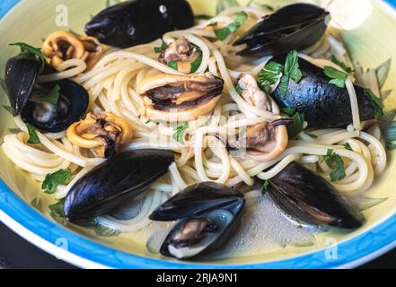 Spaghetti mit schwarzen Muscheln, Petersilienblättern und Olivenöl, serviert in einem traditionellen Keramikteller, Nahaufnahme Stockfoto