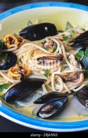Spaghetti with black mussels, parsley leaves and olive oil served in a traditional ceramic plate, close up, vertical Stockfoto