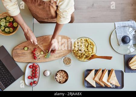Hintergrundbild der Frau, die Kirschtomaten und Brokkoli auf einem Holzschneidebrett in der Küche schneidet, während sie Pasta kocht, Kopierraum Stockfoto