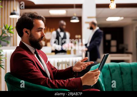 Ein Geschäftsmann, der sich auf einem Video trifft und ein Tablet für die Internetverbindung benutzt, während er auf den Check-in wartet. Unternehmer auf Geschäftsreisen ins Ausland, Ferngespräche. Stockfoto