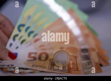 Berlin, Deutschland. August 2023. Eine Frau hält Banknoten im Wert von 100 und 50 Euro in der Hand. Eine 1-Euro-Münze liegt auf den Rechnungen. Kredit: Monika Skolimowska/dpa/Alamy Live News Stockfoto