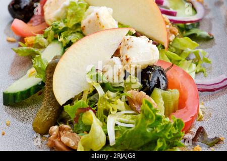 Nahaufnahme eines frischen Salats mit gegrilltem Ziegenkäse, Apfel, Sellerie, Walnüssen, Tomaten, rote Zwiebeln, Salat, Gurke, Pinienkerne, Walnüsse und Oliven Stockfoto