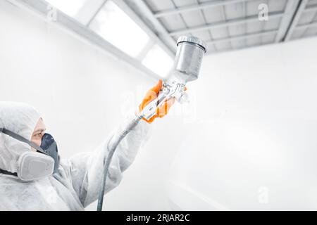 Sprühmaler im Schutzhandschuh mit Airbrush-Pulverisierer zur Lackierung der Karosserie in der weißen Lackkammer. Stockfoto