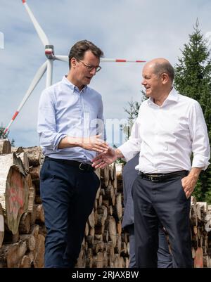 Simmerath, Deutschland. August 2023. Bundeskanzler Olaf Scholz (SPD, r) und der Ministerpräsident von Nordrhein-Westfalen, Hendrik Wüst (CDU), schütteln bei ihrem Besuch eines kommunalen Windparks die Hand. Die kleine Stadt mit mehr als 15.000 Einwohnern macht Gewinne, indem sie das Waldland in gemeinschaftlichem Besitz an den Betreiber vermietet. Ein Teil der Einnahmen fließt in den kommunalen Haushalt und ermöglicht niedrige Immobilien- und Gewerbesteuern. Quelle: Bernd Thissen/dpa/Alamy Live News Stockfoto