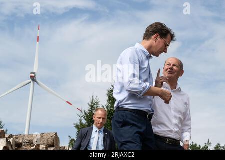 Simmerath, Deutschland. August 2023. Bundeskanzler Olaf Scholz (SPD, r) und der Ministerpräsident von Nordrhein-Westfalen, Hendrik Wüst (CDU), sprechen während ihres Besuchs in einem kommunalen Windpark. Die kleine Stadt mit mehr als 15.000 Einwohnern macht Gewinne, indem sie das Waldland in gemeinschaftlichem Besitz an den Betreiber vermietet. Ein Teil der Einnahmen fließt in den kommunalen Haushalt und ermöglicht niedrige Immobilien- und Gewerbesteuern. Quelle: Bernd Thissen/dpa/Alamy Live News Stockfoto