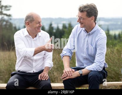 Simmerath, Deutschland. August 2023. Bundeskanzler Olaf Scholz (SPD, l) und der Ministerpräsident von Nordrhein-Westfalen, Hendrik Wüst (CDU), sprechen während ihres Besuchs in einem kommunalen Windpark. Die kleine Stadt mit mehr als 15.000 Einwohnern macht Gewinne, indem sie das Waldland in gemeinschaftlichem Besitz an den Betreiber vermietet. Ein Teil der Einnahmen fließt in den kommunalen Haushalt und ermöglicht niedrige Immobilien- und Gewerbesteuern. Quelle: Bernd Thissen/dpa/Alamy Live News Stockfoto