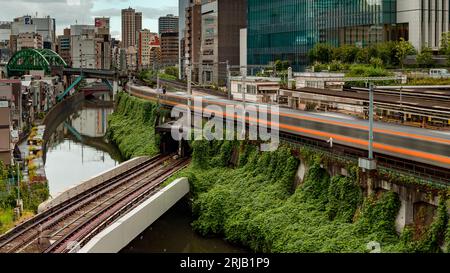 TOKIO, JAPAN - 09. AUGUST 2023: Langzeitbelichtung (verschwommene Bewegung) von U-Bahn- und Bahnzügen, die über den Kanda-Fluss an der Hijiribashi-Brücke fahren, Stockfoto