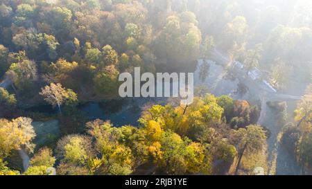 Luftfliegen über Bäume mit gelben Blättern, See, Säulen und Wanderungen an sonnigen Herbstvormittagen im Park. Helles Sonnenlicht, glänzende Sonnenstrahlen und übermäßige Sonneneinstrahlung. Wunderschöner natürlicher Hintergrund Stockfoto