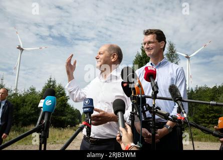 Simmerath, Deutschland. August 2023. Bundeskanzler Olaf Scholz (SPD, l) und der Ministerpräsident von Nordrhein-Westfalen, Hendrik Wüst (CDU), halten während ihres Besuchs eines kommunalen Windparks Presseerklärungen ab. Die kleine Stadt mit mehr als 15.000 Einwohnern erwirtschaftet Gewinne, indem sie die Waldflächen in gemeinschaftlichem Besitz an den Betreiber vermietet. Ein Teil der Einnahmen fließt in den kommunalen Haushalt und ermöglicht niedrige Immobilien- und Gewerbesteuern. Quelle: Bernd Thissen/dpa/Alamy Live News Stockfoto