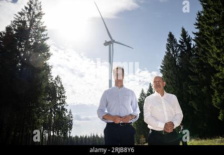 Simmerath, Deutschland. August 2023. Bundeskanzler Olaf Scholz (SPD, r) und der Ministerpräsident von Nordrhein-Westfalen, Hendrik Wüst (CDU), sprechen während ihres Besuchs in einem kommunalen Windpark. Die kleine Stadt mit mehr als 15.000 Einwohnern macht Gewinne, indem sie das Waldland in gemeinschaftlichem Besitz an den Betreiber vermietet. Ein Teil der Einnahmen fließt in den kommunalen Haushalt und ermöglicht niedrige Immobilien- und Gewerbesteuern. Quelle: Bernd Thissen/dpa/Alamy Live News Stockfoto