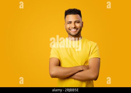 Lächelnder, selbstbewusster Indianer, der ein lässiges T-Shirt trägt, mit überkreuzten Armen isoliert auf gelb, Studioaufnahme eines fröhlichen lateinischen Geschäftsmannes, Erfolgskonzept, Kopierraum Stockfoto