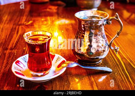 Eine Glasschale schwarzen Tees aus der Teekanne mit frischen Teeblättern, traditionelles türkisches Heißgetränk Stockfoto
