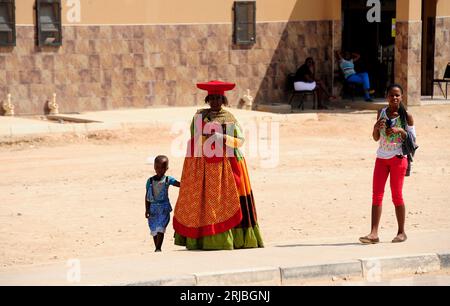 Herero-Frau mit ihrem traditionellen und farbenfrohen Kleid im Kontrast zu einem Mädchen in einem modernen oder abendländischen Kleid. Nord-Namibia. Stockfoto