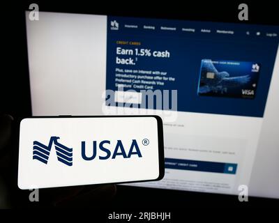 Person holding mobile phone with logo of United Services Automobile Association (USAA) on screen in front of web page. Focus on phone display. Stock Photo