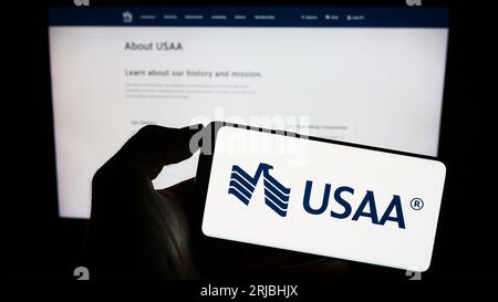 Person holding smartphone with logo of United Services Automobile Association (USAA) on screen in front of website. Focus on phone display. Stock Photo
