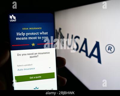 Person holding mobile phone with web page of United Services Automobile Association (USAA) on screen with logo. Focus on center of phone display. Stock Photo
