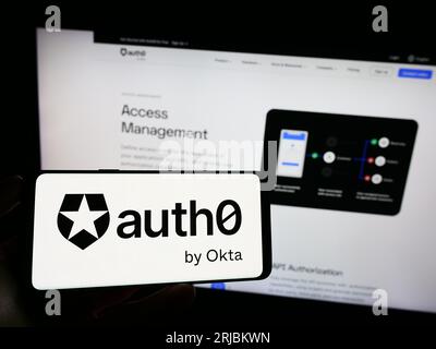 Person holding cellphone with logo of US identity platform company Auth0 by Okta on screen in front of business webpage. Focus on phone display. Stock Photo