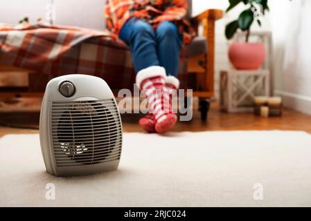 Elektrische Heizung mit Ventilator auf dem Boden im Wohnzimmer mit menschlichem Sitzen auf dem Sofa im Hintergrund Stockfoto