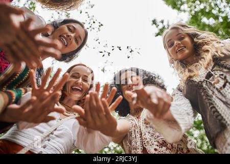 Blick von unten auf positive und trendige interrassische Frauen, die im Retreat Center vor der Kamera winken Stockfoto