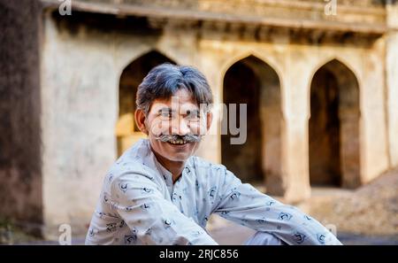 Ein indischer Mann mit einem Schnurrbart, der an einer Wand im Ranthambore Fort im Ranthambore National Park in Rajasthan, Nordindien, sitzt Stockfoto