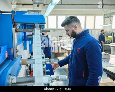 Mitarbeiter, die in einer Etikettendruckerei arbeiten. Der Arbeiter verwendet eine Etikettiermaschine. Aufkleberdrucker. Druckmaschine, die an Etiketten arbeitet. Stockfoto