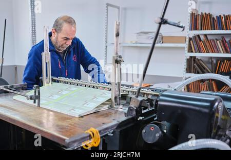 Mitarbeiter, die in einer Etikettendruckerei arbeiten. Der Arbeiter verwendet eine Etikettiermaschine. Aufkleberdrucker. Druckmaschine, die an Etiketten arbeitet. Stockfoto