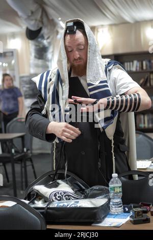 Ein orthodoxer jüdischer Mann zieht seine Tefillin an und passt sie vor dem Morgengottesdienst an. Im Rockland County, New York. Stockfoto