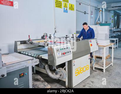 Mitarbeiter, die in einer Etikettendruckerei arbeiten. Der Arbeiter verwendet eine Etikettiermaschine. Aufkleberdrucker. Druckmaschine, die an Etiketten arbeitet. Stockfoto