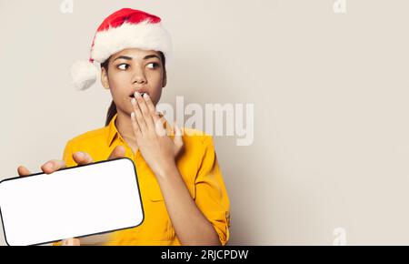 Weihnachtsporträt einer hübsch überraschten Weihnachtsfrau, die ein Smartphone mit leerem weißen Bildschirm auf weißem Hintergrund hält Stockfoto