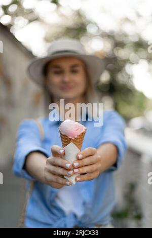 Sommerdessert und fröhliches Sommerkunstkonzept. Gesundes veganes Erdbeereis-Eis-Eis in der Hand einer jungen Frau im Hintergrund Stockfoto