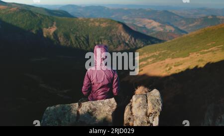 Girl Travel Bloggerin auf dem Berggipfel genießen Sie die Natur aus der Luft. Frau, die auf Felsen sitzt und sich die Hände erhebt, genießt das Wandern. Freiheit freudige Spannung von Stockfoto