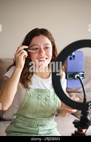Glücklicher Influencer, der zu Hause Make-up-Tutorial auf dem Smartphone aufnimmt Stockfoto