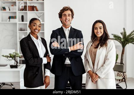 Drei multiethnische Geschäftsleute, die in modernen Büros in Innenräumen stehen und vor der Kamera lächeln Stockfoto