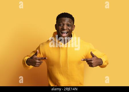Aufgeregter junger Schwarzer mit gelbem Hoodie, der auf sich selbst zeigt Stockfoto