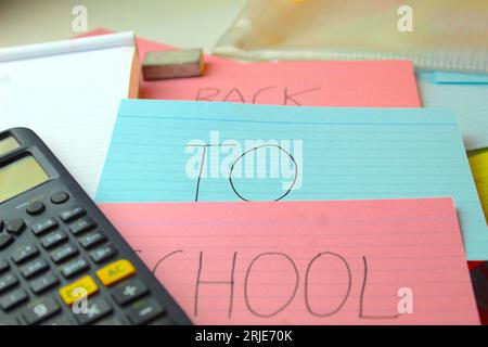 Ein Foto der Worte „zurück zur Schule“ auf farbigen Karteikarten auf einem Schreibtisch mit Taschenrechnern, Gummis und Ordnern. Stockfoto