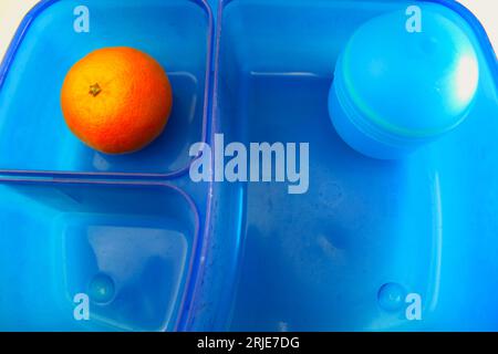 Ein Foto einer blauen Lunchbox für einen Schüler mit einer Orange darin. Stockfoto