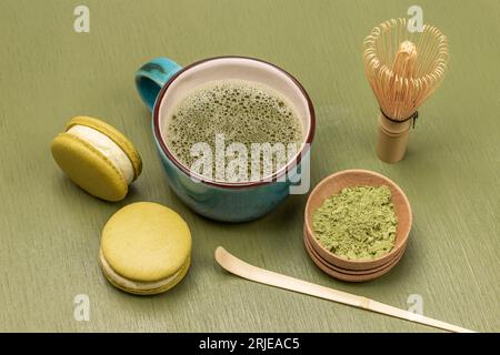 Macaron-Kuchen und eine Tasse Matcha-Tee. Schneebesen, Bambuslöffel und Matcha-Teepulver in einer Holzschale. Draufsicht. Grüner Hintergrund Stockfoto