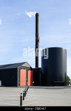 Moderne Fabrik mit einem hohen rostigen Schornstein, aus dem weißer Dampf auf blauem Himmelshintergrund und Schornstein am Himmel austritt Stockfoto