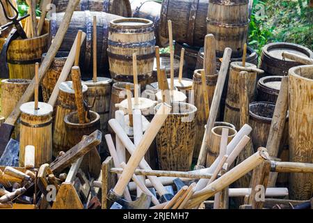 Alte, traditionelle Holzfässer in verschiedenen Größen mit Metallreifen, verschiedenen Holzbutterwürfeln, Holzutensilien und Werkzeugen Stockfoto
