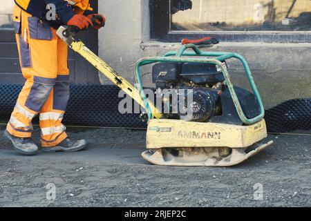 Poznan, Polen - 21. April 2023: Ein Arbeiter verdichtet den Asphaltboden mit Spezialausrüstung. Nahaufnahme. Stockfoto