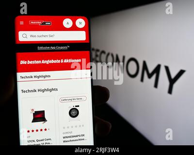 Person, die ein Smartphone mit der Webseite des deutschen Einzelhandelsunternehmens CECONOMY AG auf dem Bildschirm vor dem Logo hält. Konzentrieren Sie sich auf die Mitte der Telefonanzeige. Stockfoto