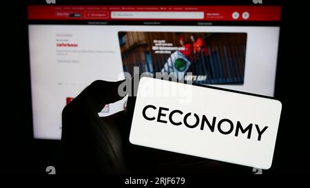 Person, die ein Mobiltelefon mit dem Logo des deutschen Einzelhandelsunternehmens CECONOMY AG auf dem Bildschirm vor der Business-Webseite hält. Konzentrieren Sie sich auf das Display des Telefons. Stockfoto