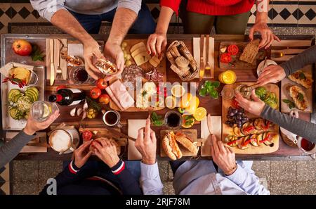 Blick von oben auf anonyme Menschen, die leckere Speisen essen, während sie am Holztisch mit verschiedenen Vorspeisen in der hellen Küche sitzen Stockfoto