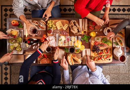 Blick von oben auf anonyme Menschen, die leckere Snacks mit Gemüse essen, während sie am Tisch mit Getränken in der Küche zu Mittag essen Stockfoto