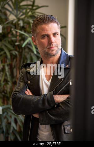 Hübscher reifer bärtiger Mann in Lederjacke mit stylischem Haarschnitt, der die Kamera anschaut, während er mit überkreuzten Armen steht Stockfoto